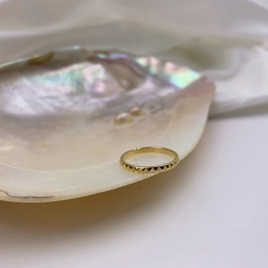 Detailed close-up of gold geometric pyramid textured ring displayed on a white shell edge