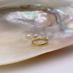 Macro shot of gold-plated pyramid textured ring on iridescent pearl shell backdrop
