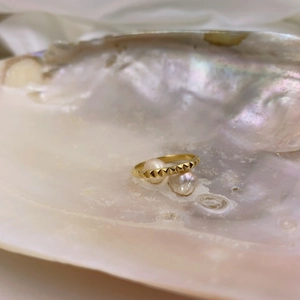 Macro detail of gold pyramid textured ring resting on a lustrous iridescent pearl shell