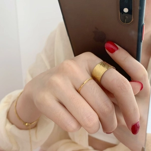 Close-up of a wide 18K gold plated textured band ring and fine chain bracelet