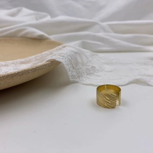 Golden wide band ring with textured diagonal patterns on elegant white lace background