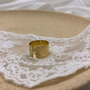 Macro detail of wide gold adjustable ring with vintage tree bark texture on lace background