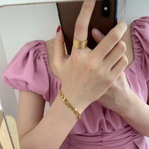 Close-up of golden wide textured ring and flat cuban chain bracelet on hand