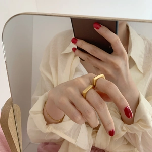 Mirror selfie showing two gold geometric rectangular rings and a minimalist bangle on hand