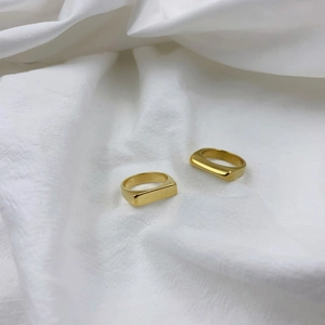Detailed view of two minimalist polished gold titanium rings on a soft white fabric background