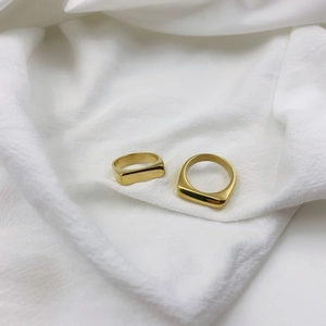 Close-up of two polished gold stainless steel signet rings on a soft white fabric background