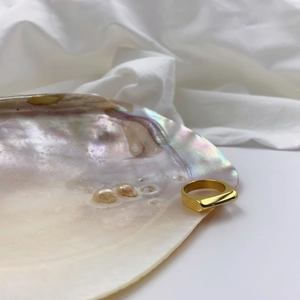 Detailed view of a glossy gold signet ring displayed on a natural seashell with pearls