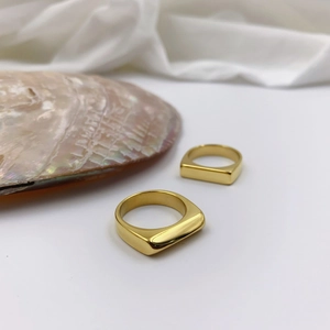 Detailed view of two minimalist gold geometric signet rings on a white silk surface