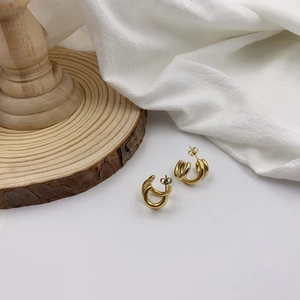 Close-up of golden triple-layered irregular geometric hoop earrings on white linen fabric