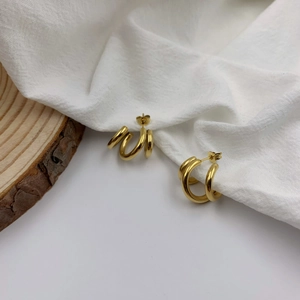Detail of overlapping golden geometric triple-hoop earrings on white textured linen