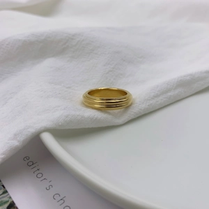 Detailed close-up of a gold triple-layered textured ring on white soft fabric