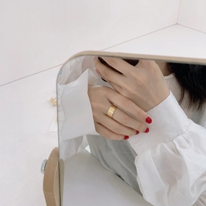 Macro view of wide gold brushed ring on finger paired with white ruffled sleeve shirt