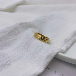 Detail of a minimalist triple-layer gold ring resting on soft white textured linen fabric