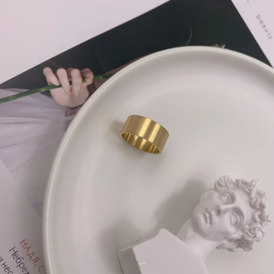 Modern wide gold ring with brushed finish displayed on white porcelain and art background