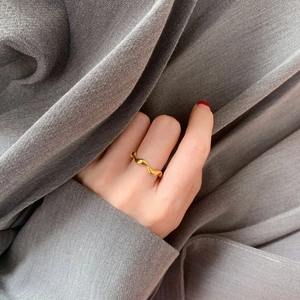 Close-up of a minimalist gold wave ring on hand against a dark textured fabric background