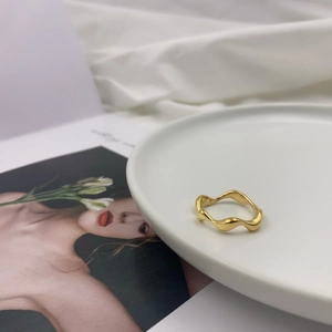 Detail of a wave-shaped irregular gold ring leaning on a white ceramic plate background