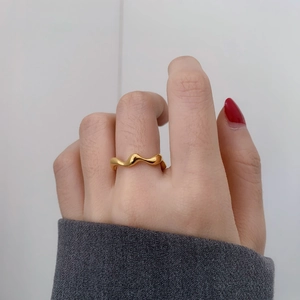 Close-up of a minimalist golden wavy ring with high polish finish worn on index finger