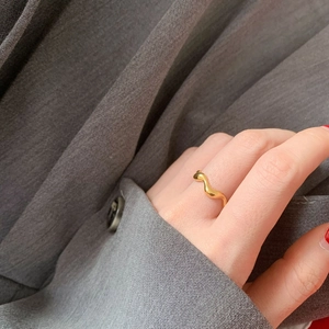 Close-up of minimalist gold wave ring showing smooth lines on a grey suit fabric