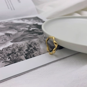 Detailed close-up of a polished gold wavy ring leaning against a ceramic tray