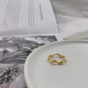 Close-up of a polished gold wavy irregular ring placed on a white ceramic plate