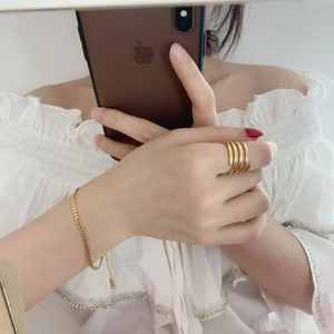 Detail view of a multi-layer spiral gold ring and textured wheat chain bracelet on hand