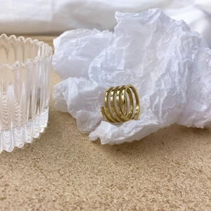 Detail of a minimalist multi-layered gold spiral ring on a white textured background