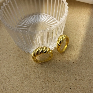 Gros plan de deux bagues croissantes dorées avec texture nervurée sur fond beige