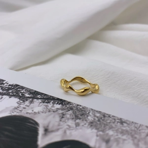 Minimalist gold wavy ring with irregular fluid design on white textured fabric background