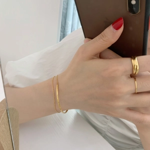 Detail of 18K gold plated double chain bracelet and minimalist rings on a person