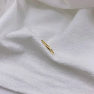 Detailed view of an 18K gold plated minimalist ultra-slim ring on a white fabric background