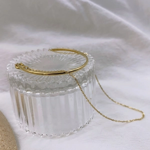 Detail of 18K gold-plated double-layer bracelet with chain and curved bar on glass