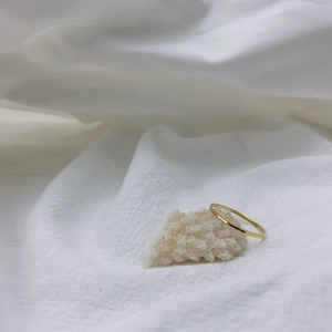 Close-up of minimalist 18K gold plated ultra-thin band ring on white coral stone