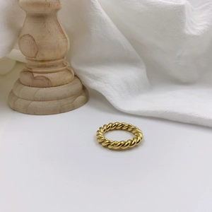 Detailed close-up of a gold twisted rope ring on a minimalist rustic wooden base