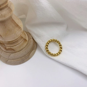 Detail shot of a golden twisted rope textured ring on white pleated fabric background