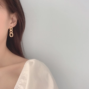 Detail shot of a minimalist gold metal chain earring worn by a model in a retro style