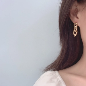 Close-up of chunky gold chain link earrings in polished metal on a model's ear