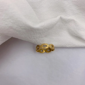 Vue rapprochée d'une bague à maillons dorée et polie sur un tissu blanc