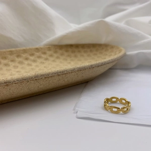 Gros plan d'une bague chaîne dorée ajourée sur fond blanc avec texture lin