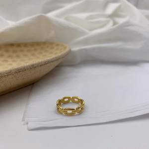 Détail d'une bague à maillons dorés présentée sur une assiette en céramique minimaliste