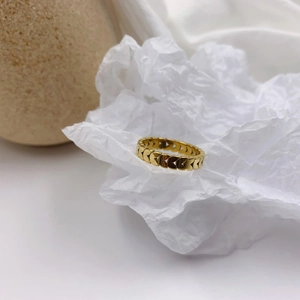 Close-up of golden hollow heart chain ring on white textured paper with soft shadows