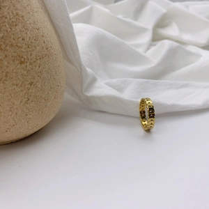 Detail view of gold openwork heart pattern ring on a minimalist textured surface