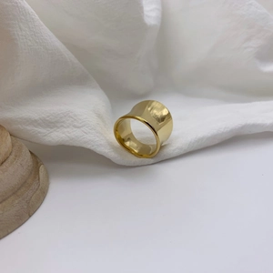 Macro detail of glossy gold irregular wide ring resting on soft white pleated fabric
