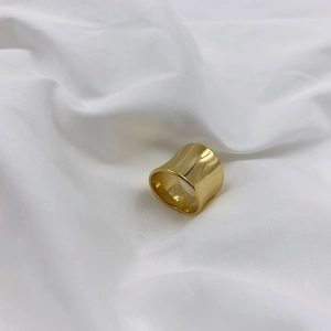 Detail of a wide gold-plated ring with polished concave surface on white fabric