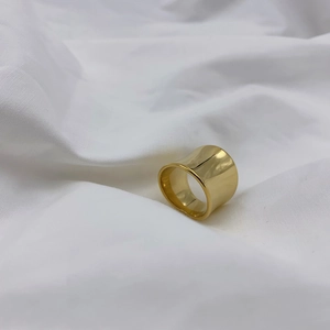 Polished wide gold band ring with irregular minimalist concave design on white fabric