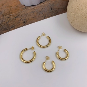Minimalist C-shaped gold hoop earrings in two sizes displayed on a modern neutral surface