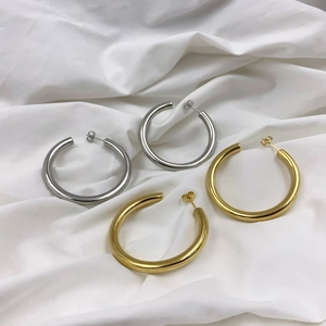 Detailed view of polished thick C-shaped hoop earrings in gold and silver on white fabric
