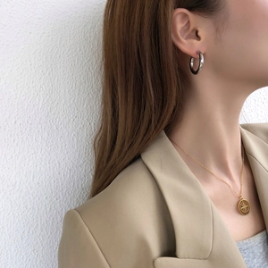Close-up of minimalist silver hoop earrings and gold compass star necklace on model