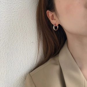 Close-up of model wearing thick silver C-shaped hoop earrings with polished metal finish