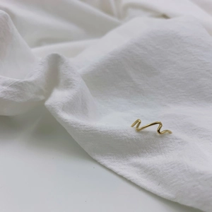 Detailed macro view of gold minimalist wave ring on white textured fabric background