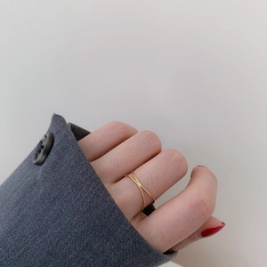 Close-up of minimalist gold double-layer cross ring worn on index finger with blazer